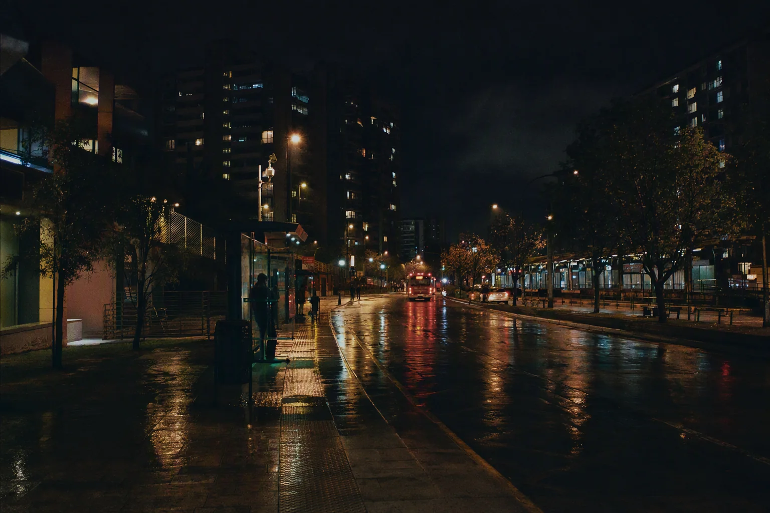 Corredor urbano contemporáneo bajo la lluvia, con transporte y luminarias activas