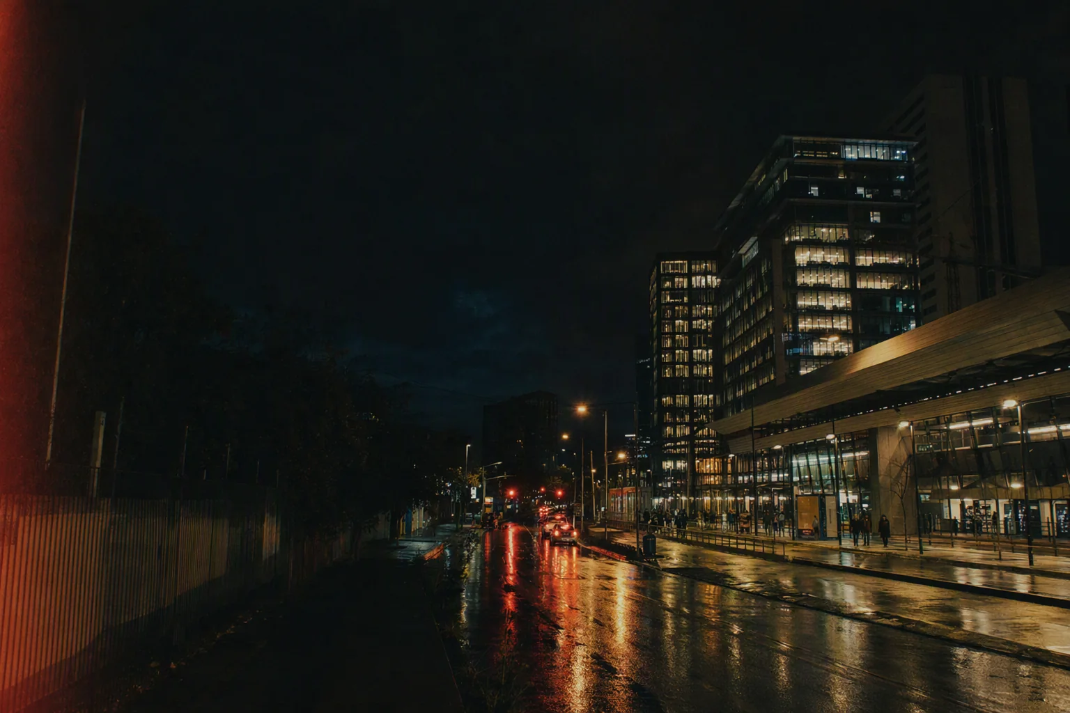 Calle urbana contemporánea de noche, con ventanas encendidas y pavimento mojado